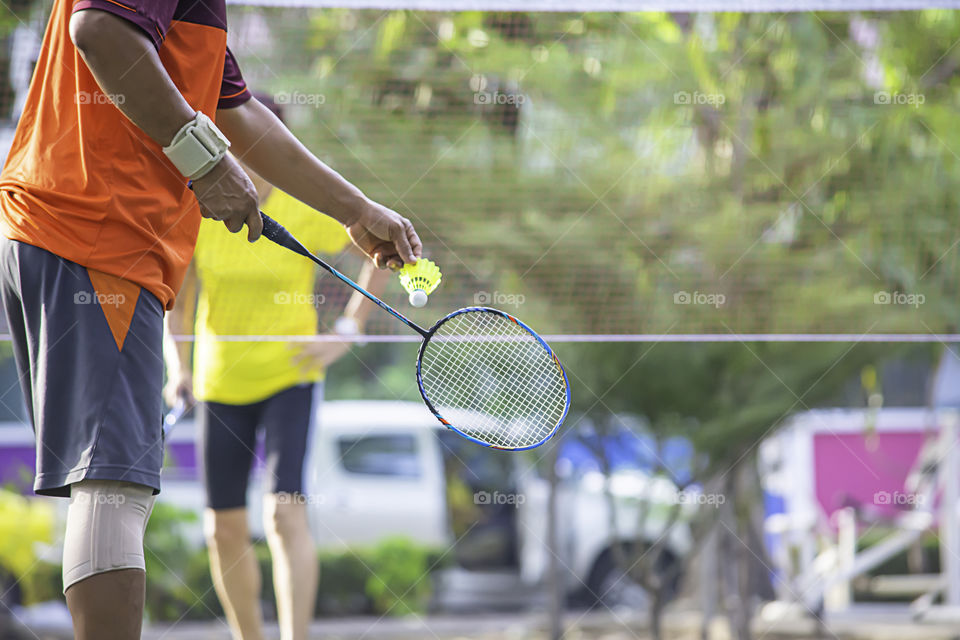 Elderly man Hand holding a badminton racket Background blur tree in park.