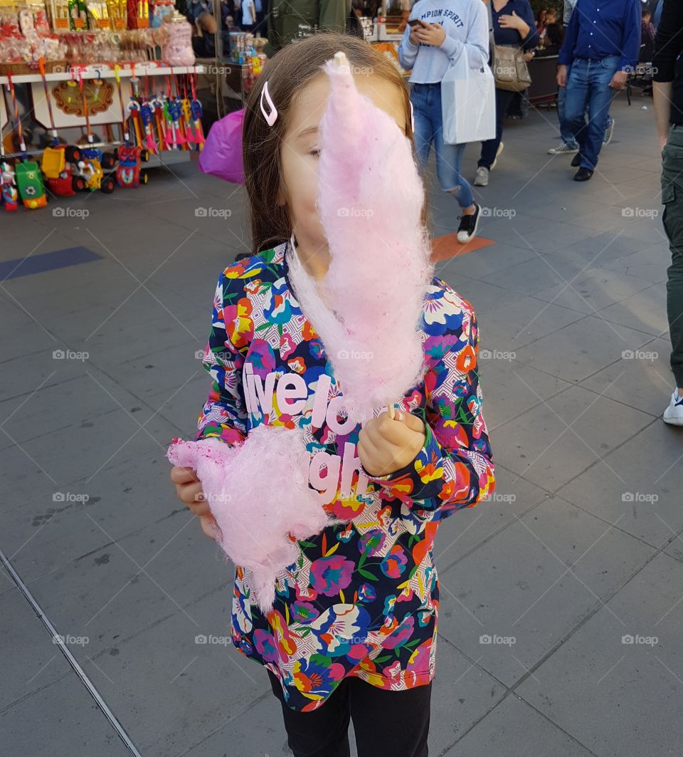 Little girl eating pink cotton candy in street market