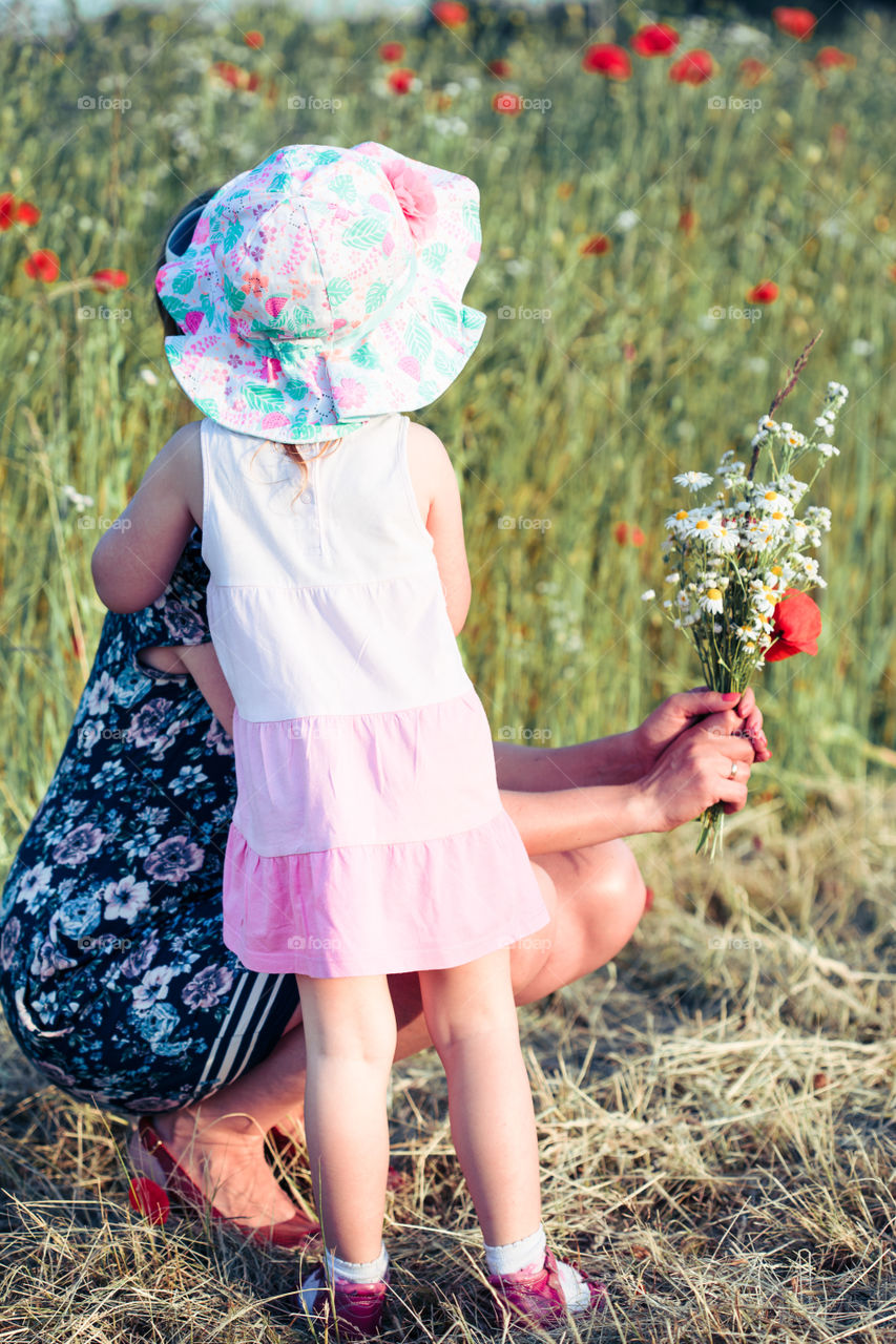 Mother and her little daughter in the field of wild flowers. Little girl picking the spring flowers for her mom for Mother's Day in the meadow. Girl handing the flowers to her mom. Nature scene, family time