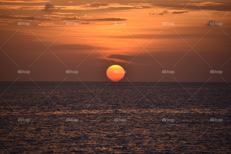 The picture captured the moment where the sunset finally hit the horizon of the sea. There is a beautiful orange and yellow sky clouded sky over a dark rippling sea in the Carribean Island of Nassau.