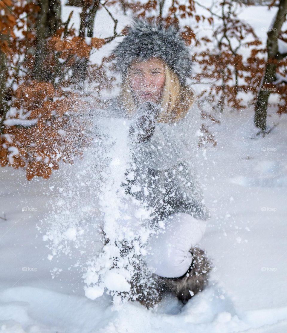 Blowing in the wind . 
snowing in the wind . 
Teenager blows  snow in the winterlandscape.