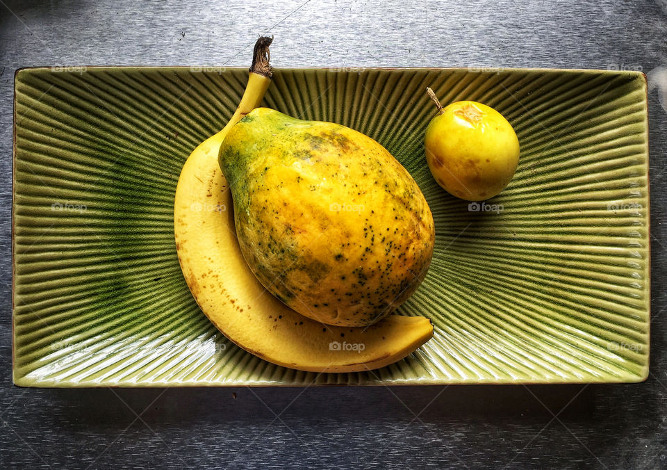 A banana, papaya and quince on a ceramic plate
