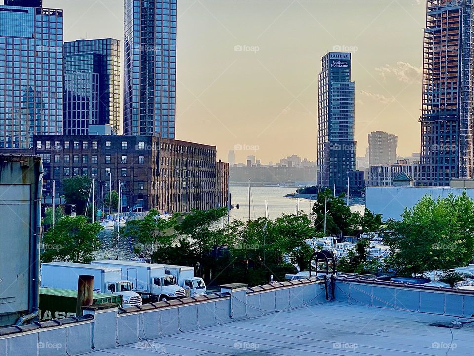This is a view of a large brownstone building in „Greenpoint“, Brooklyn seen from the staircase of the „Pulaski Bridge“ at about half level. Across the water of the „East River“ in the far distance you can see „Manhattan“. 2023. Hypnotic Productions
