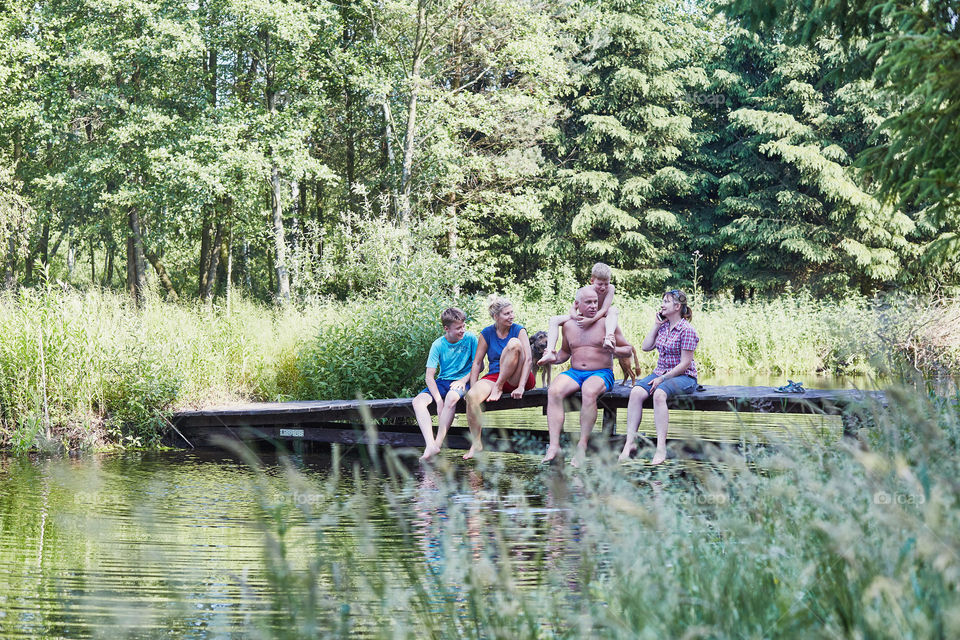 Family spending time together sitting on a bridge over a lake, among the trees, close to nature, during summer vacations. Candid people, real moments, authentic situations