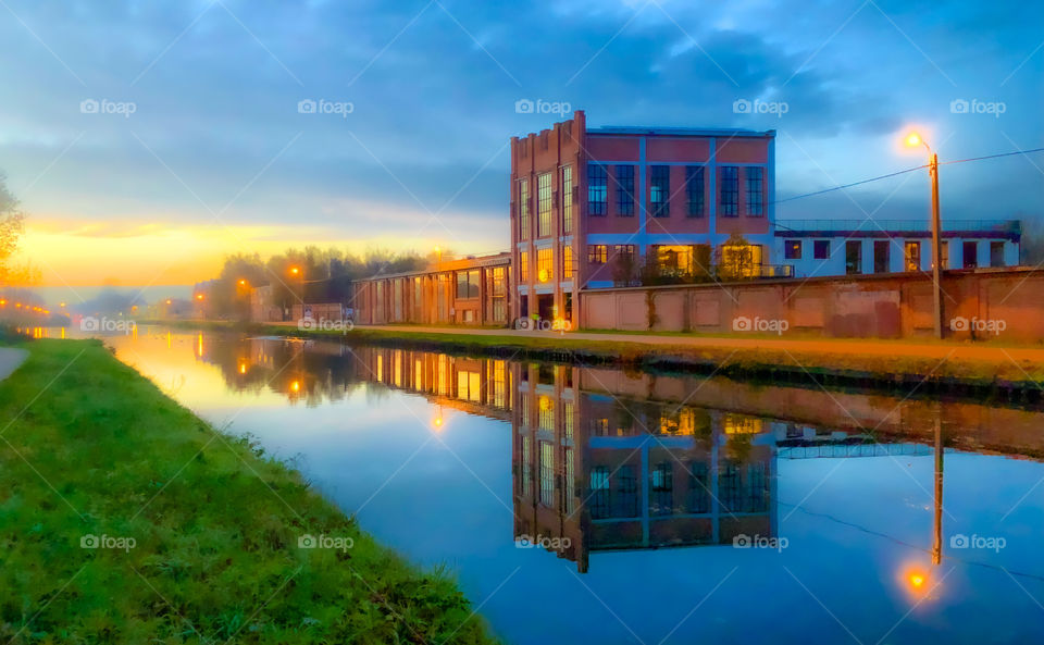 Old factory building reflected in the water of the river or canal during sunrise or sunset in a rural landscape