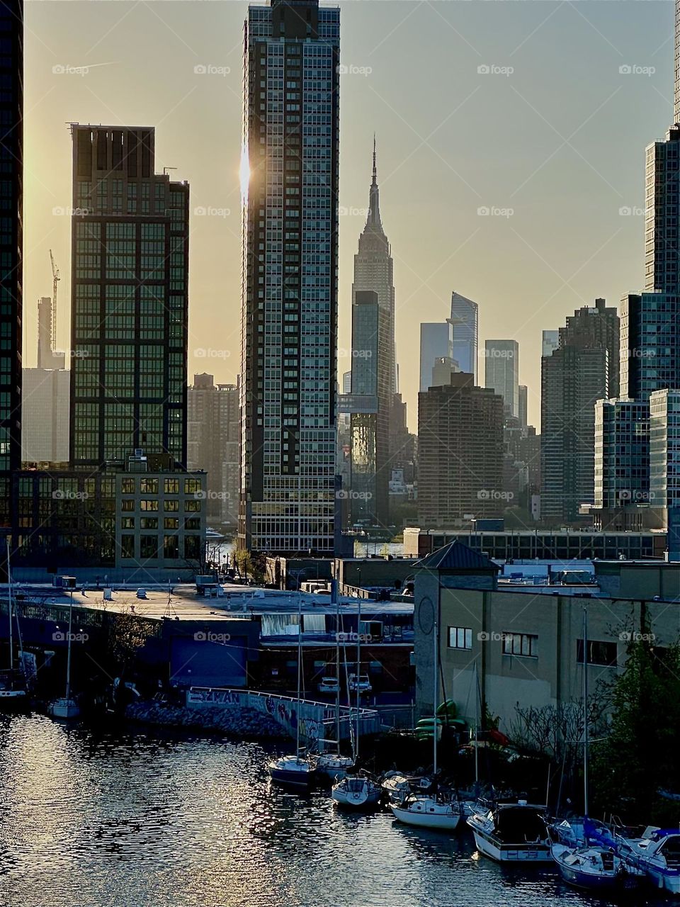 Shimmering in tones of silver and gold NYC is amazing in the setting sun seen from the „Pulaski Bridge“ at „Newtown Creek“ that connects „Greenpoint“, Bklyn to LIC, Queens. This is „Manhattan“ and the „Empire State Bldg“. 2024. Hypnotic Productions