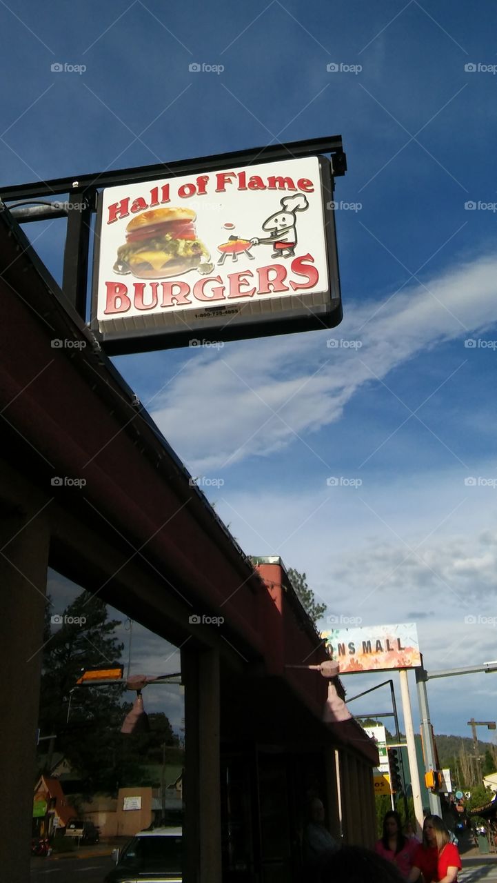 Hall of Flame Burgers, street side view of restaurant sign for diner in the small town of Ruidoso, New Mexico.  Backed with a deep blue sky with streaks of white clouds