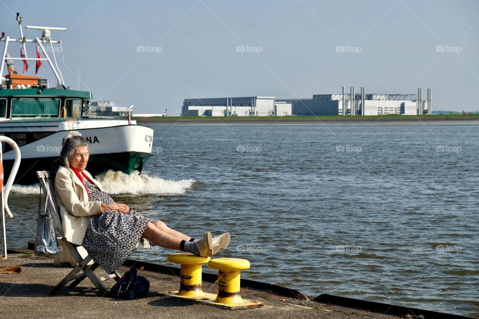 An elderly woman rests on the edge of the pier on the Elbe coast. Hamburg Blagkenese. Germany