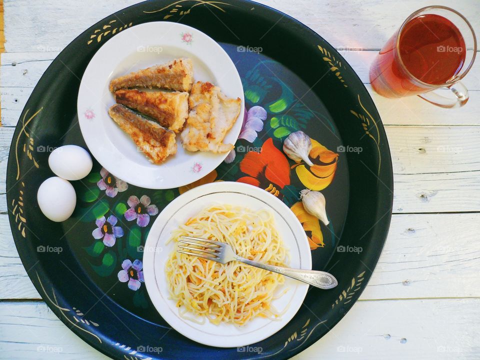 noodles in a dish, homemade cake, fried fish and a cup of tea on the table