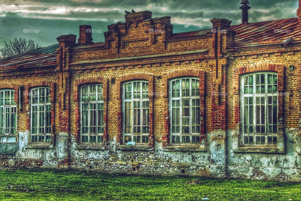 ancient brick buildings with openwork windows, cornices and a roof dot large white windows dot peeling paint cracked brick. green lawn at the base of the building.