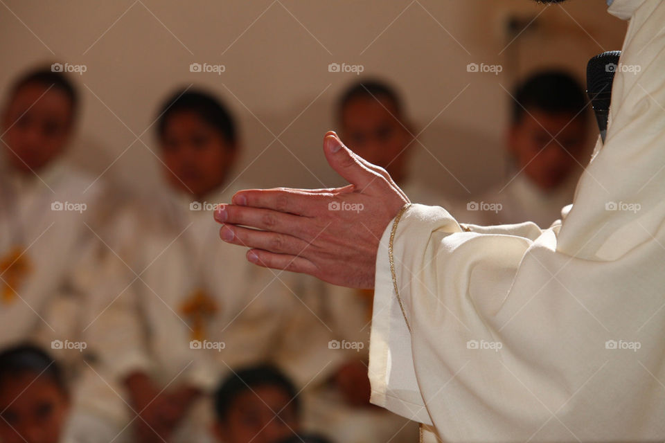 Priest holding hands together for a prayer. Kids watching behind