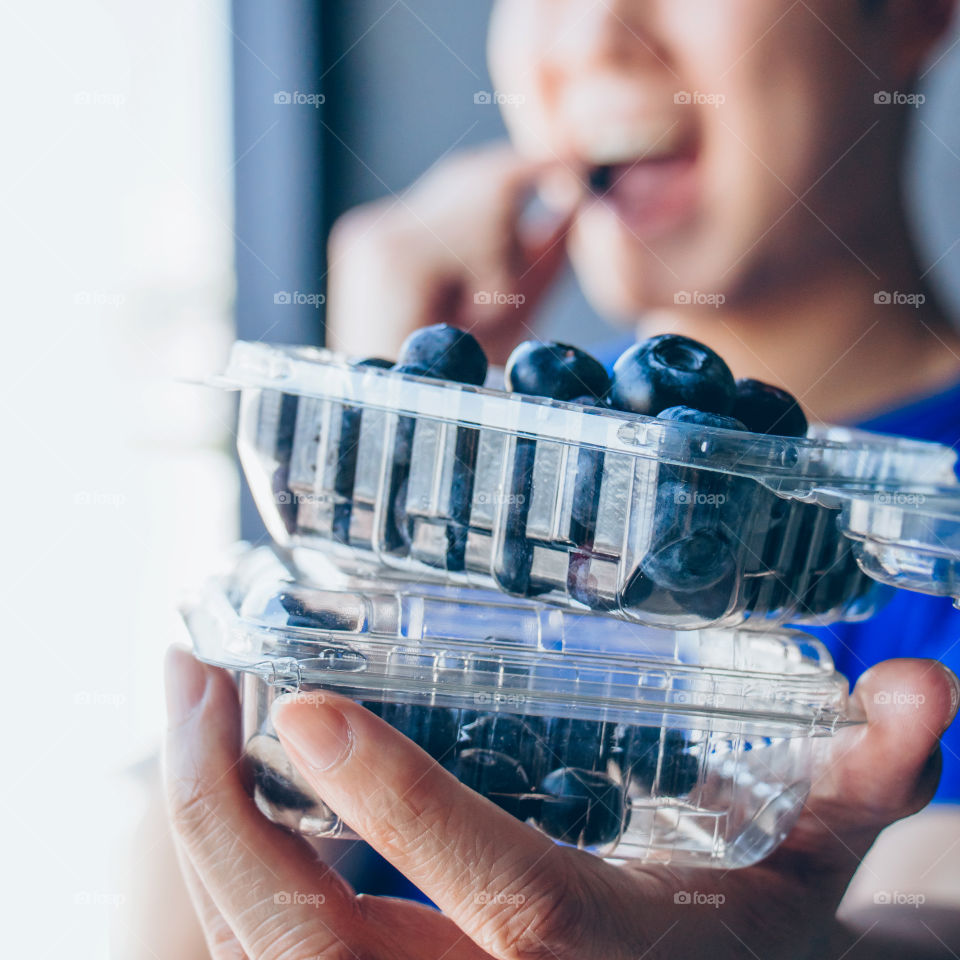 Young man holding and eating fresh blueberries in a plastic box