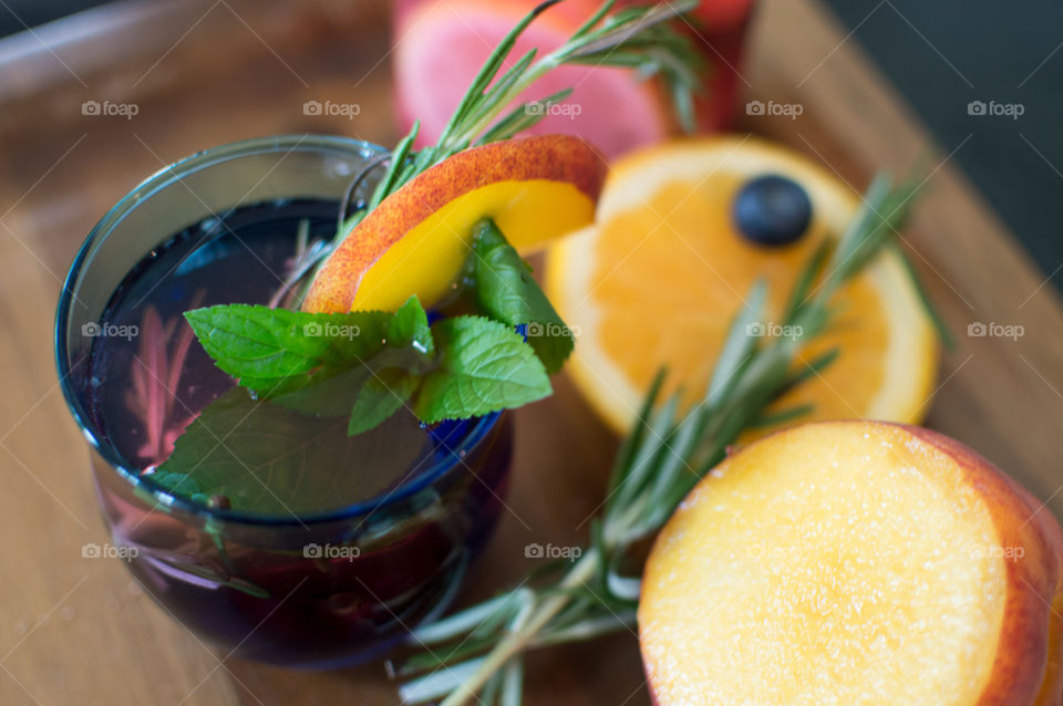 Glass of beautiful homemade juice and detox drink with peach, blueberry, mint and rosemary herbs conceptual healthy lifestyle and flavored water gourmet food photography on dark wood 