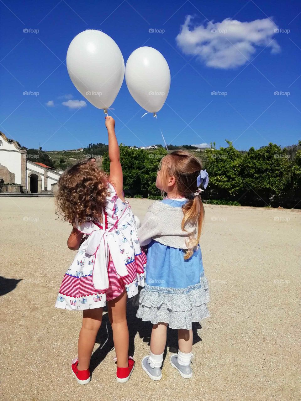 Two little girls holding their balloons in a beautiful landscape scenery.. Summertime is here