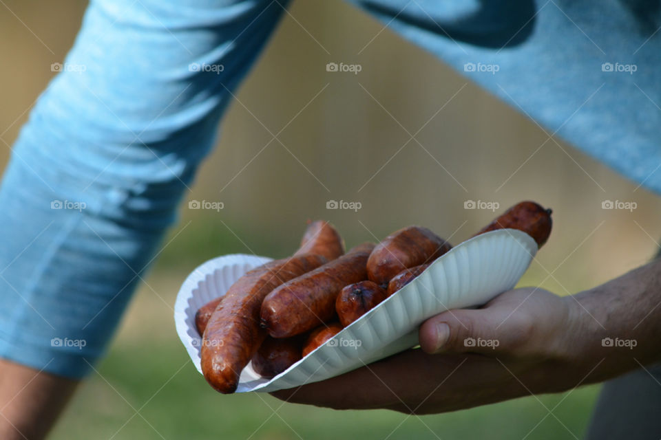 A person holding a plate of sausage
