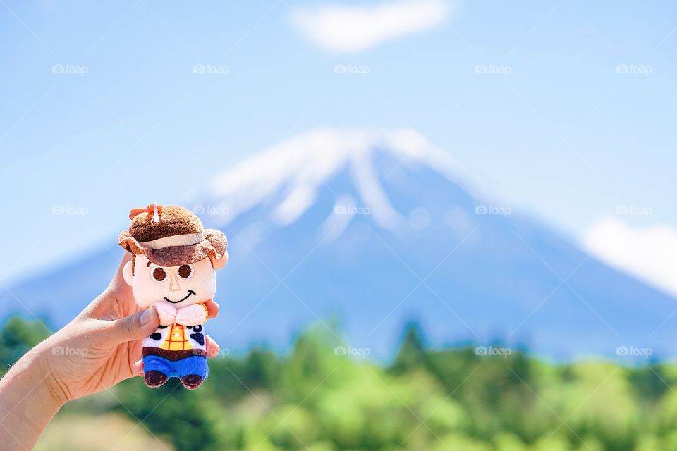 Yamanashi, Japan - May 14, 2018 : A photo of hand holding a cute plush doll of Woody, famous character from Toy Story animation with the background of Fuji Mountain or Fuji yama. Editorial use only.