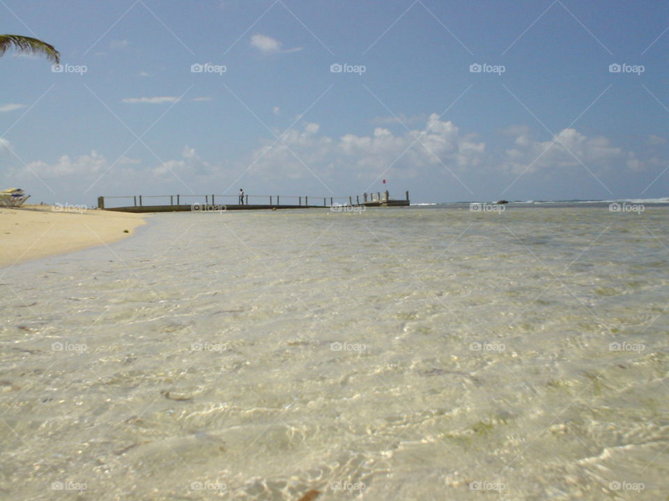 Crystal clear Caribbean waters, so serene. A long wooden pier on the horizon of a perfect blue sky.