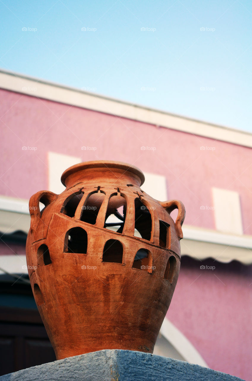Clay jar against pink wall and blue sky- Santorini, Greece