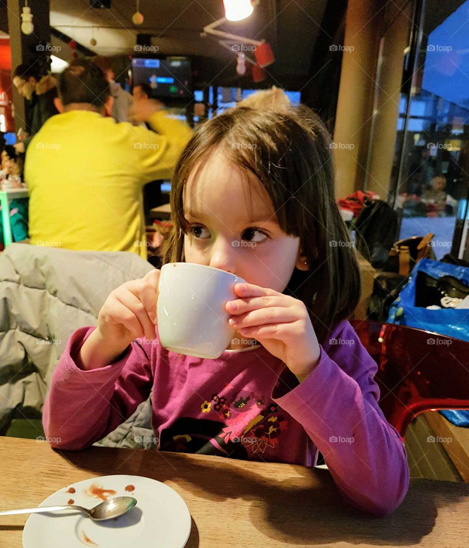 Little girl drinking coffee in restaurant