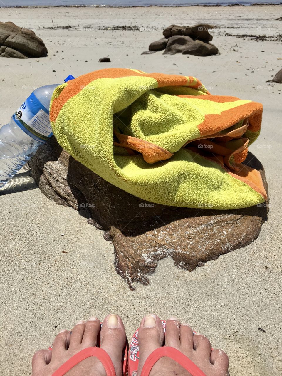 Orange beach towel on rocks at remote sandy beach 