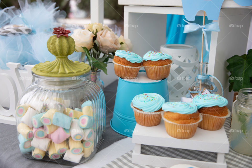 Tasty handmade freshly baked muffins with cream and colorful toppings, arranged on tray. 