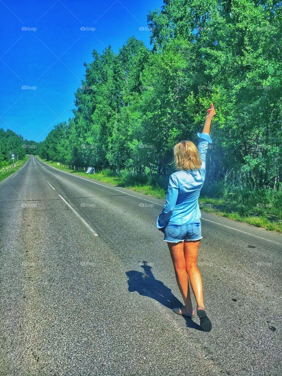 девушка блондинка идет спиной по пустой автомобильной трассе