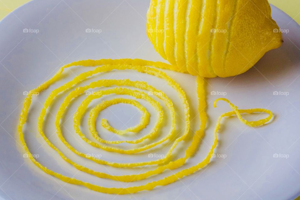 Lemon and spiraled lemon peel on a white plate with yellow background  