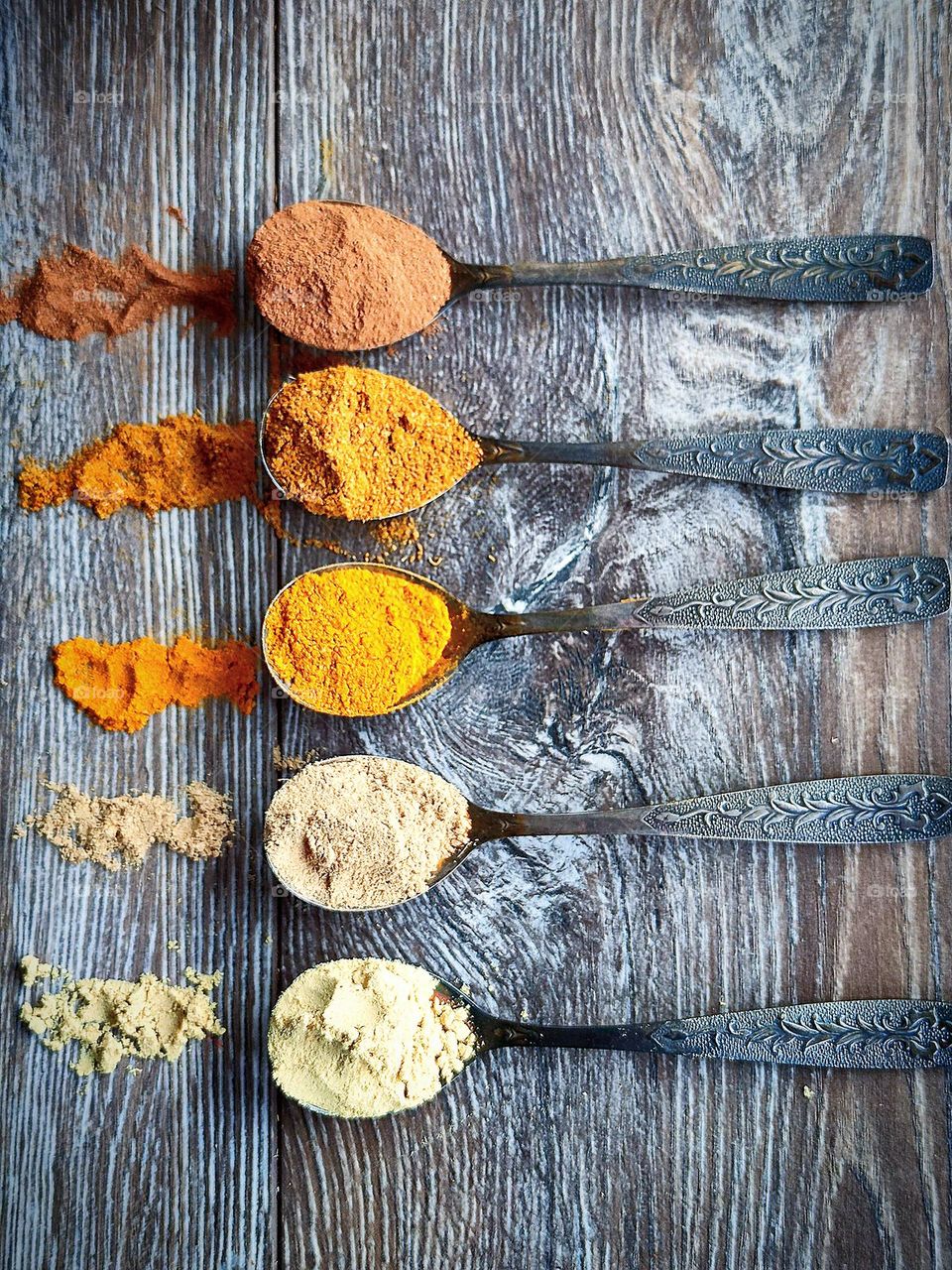 Yellow color.  All shades of yellow: from pale yellow to dark yellow.  On a wooden background are five spoons with spices: ground ginger, ground mustard, curry, turmeric and ground cinnamon.  Spices are scattered around each scoop of a spoon.