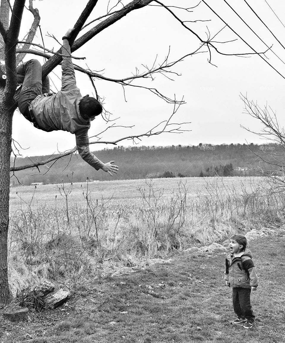 Boy looking at teenager climbing bare tree
