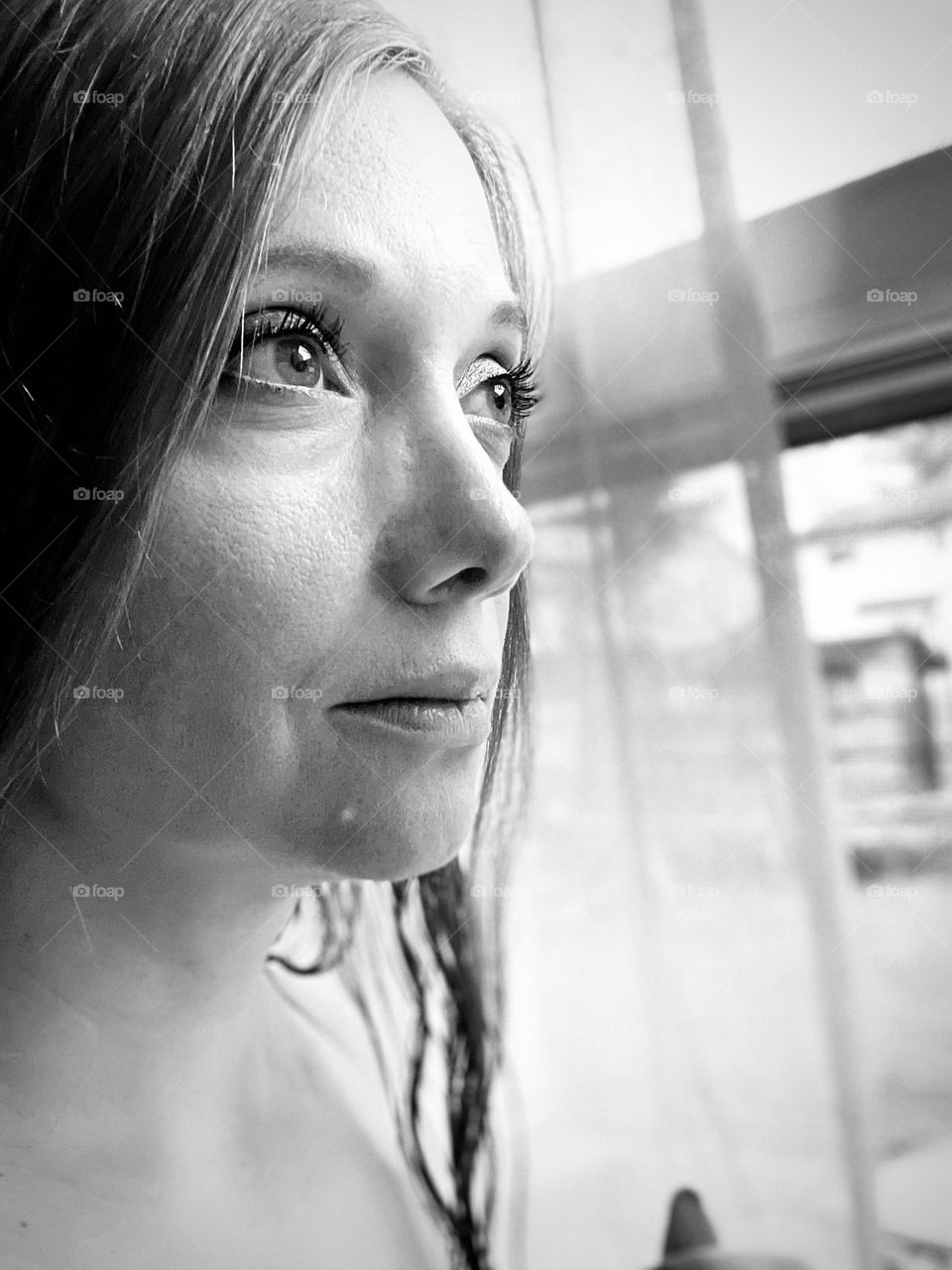 Black and white photo of woman peering out window