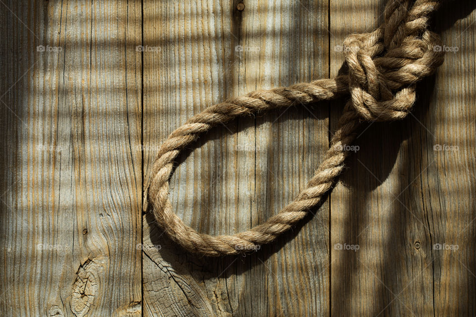 Rope with a knot on a wooden surface. Sun shines through jalousie window.