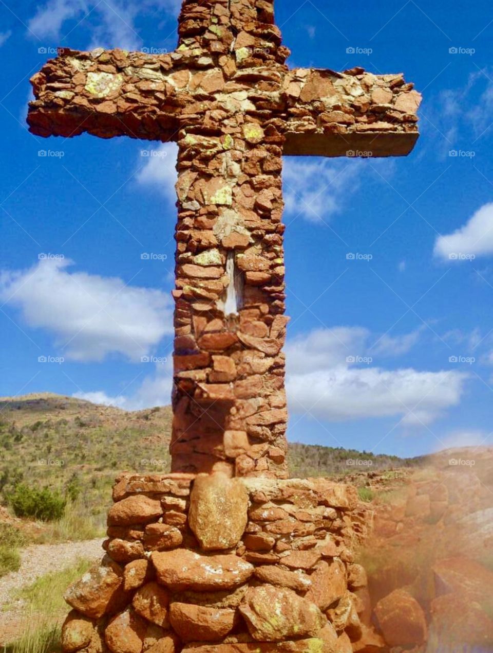 Stone cross at Holy City in the Wichita Wildlife Refuge in Oklahoma. The blue sky and white fluffy clouds are the ideal backdrop. 