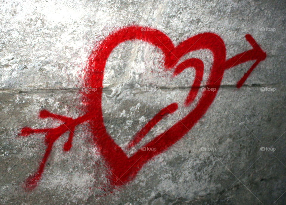 Graffito red heart with arrow, in love, on a stone wall