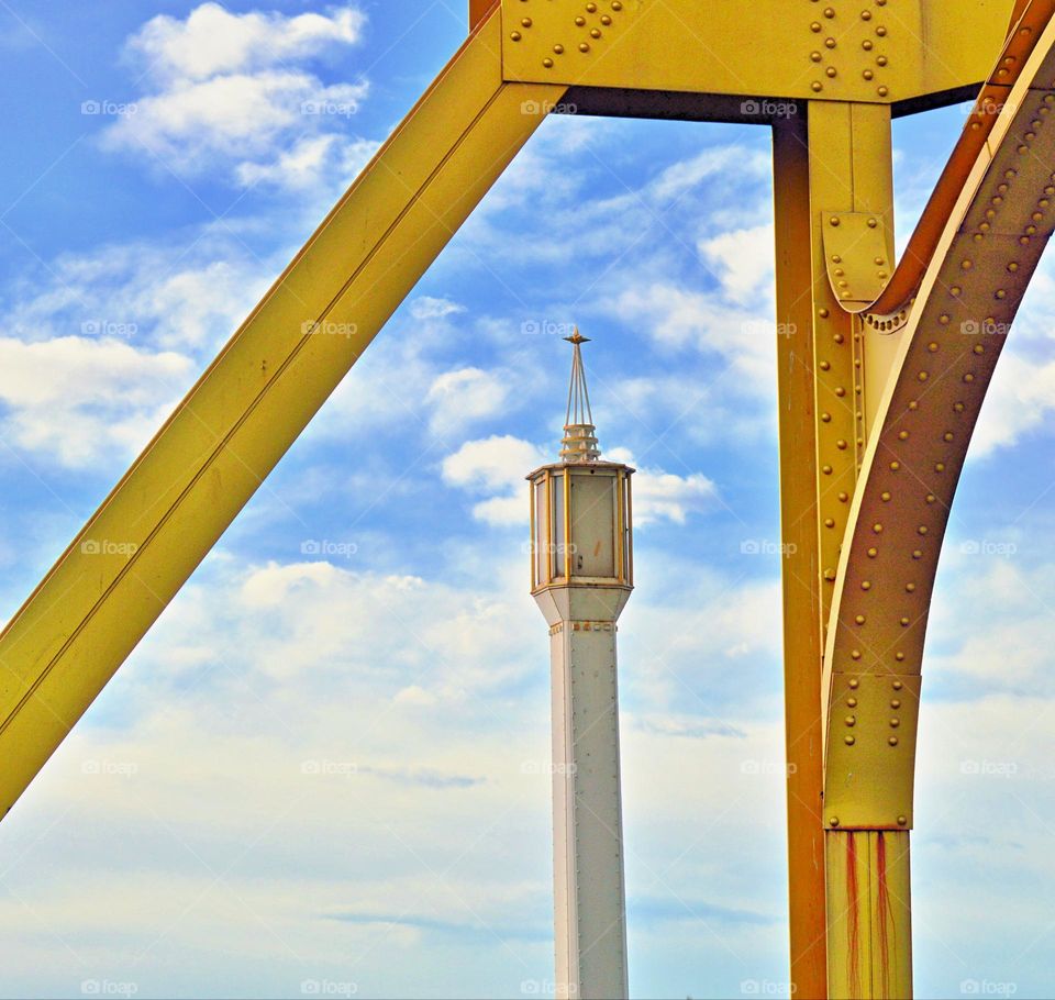Golden metal Bridge with a metal golden lamp post with cloudy blue skies in the background