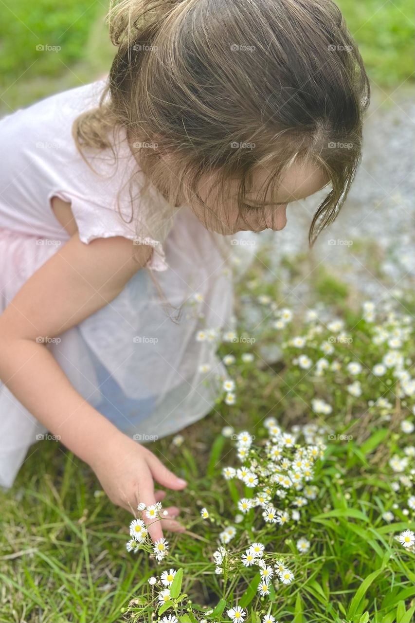 A young girl kneels down to examine small white flowers in a yard during the Spring season