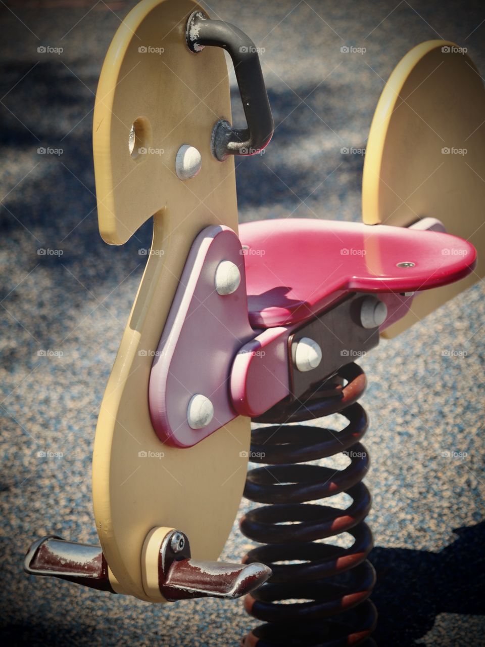 A metal rocking toy in the shadows of a children’s playground on a warm spring day