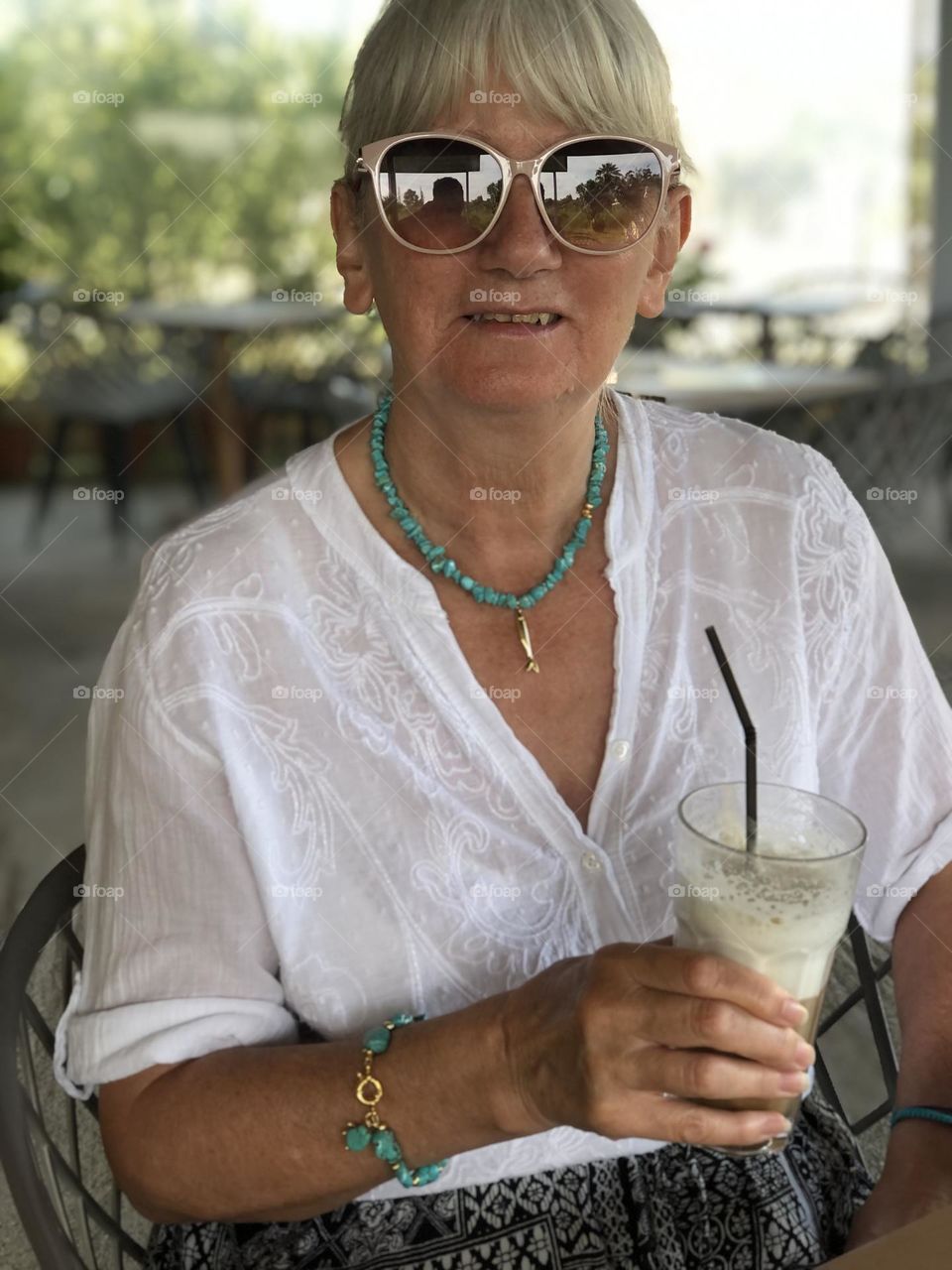 Female wearing sunglasses, holding a drink, smiling, happy. Coffee 