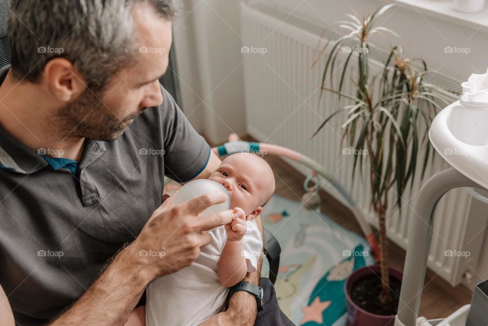 Father feeding his baby son with bottle of baby formula