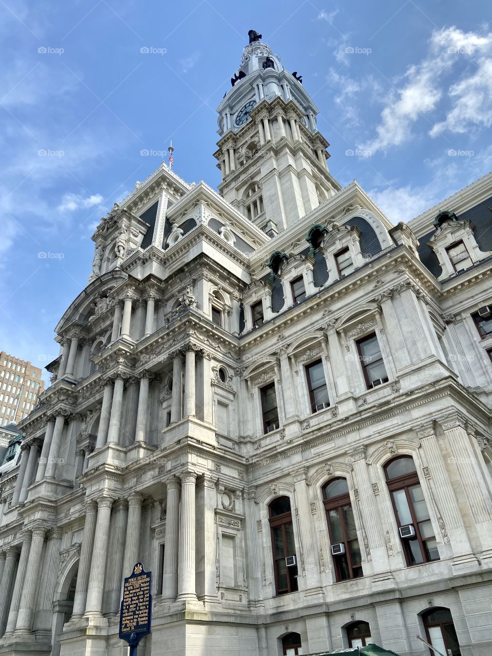 Looking up at a tall very ornate concrete historical building against a blue sky with white clouds 