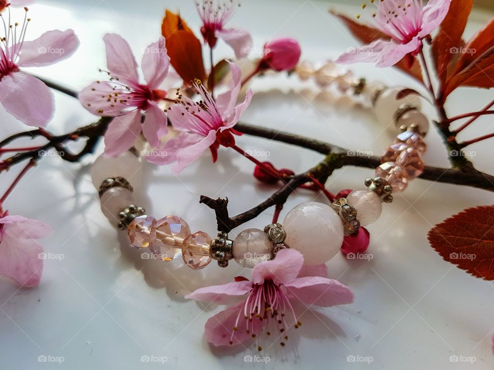 Jewellery and flower mix. Pink blossom flower tree branch, with a cream pearl and diamond bracelet. On white background.