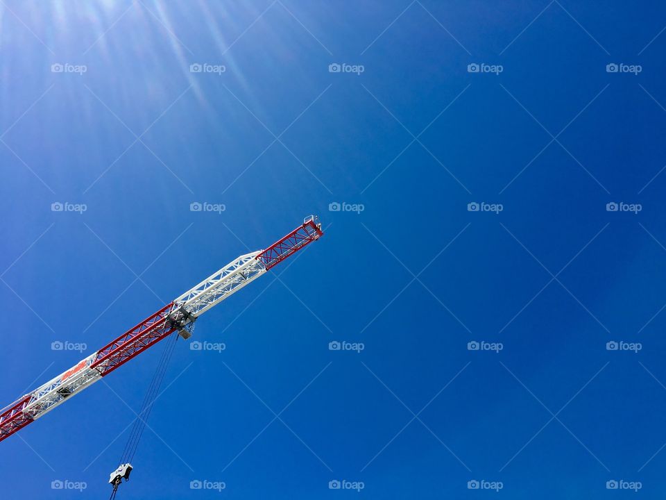 Red and white steel construction crane high in the air against a vivid blue sky minimalistic 