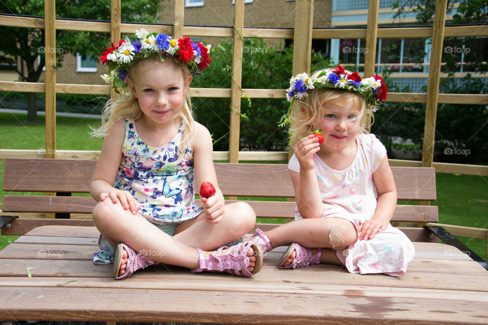 Sisters sitting on bench eating strawberries