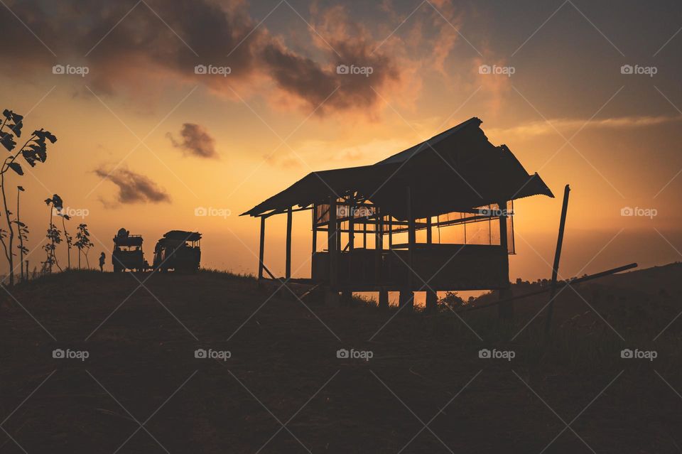 Sunset over the hills with the view of silhouette of trucks, people and an abandoned house