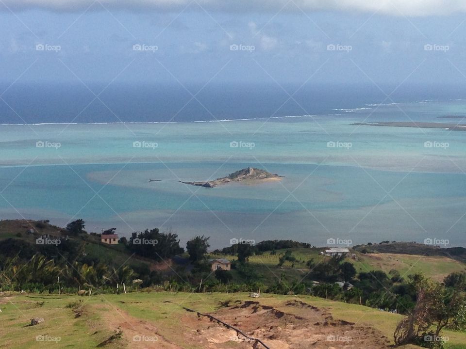 Lagon avec une petite île au centre dans un océan bleu turquoise depuis le rivage 