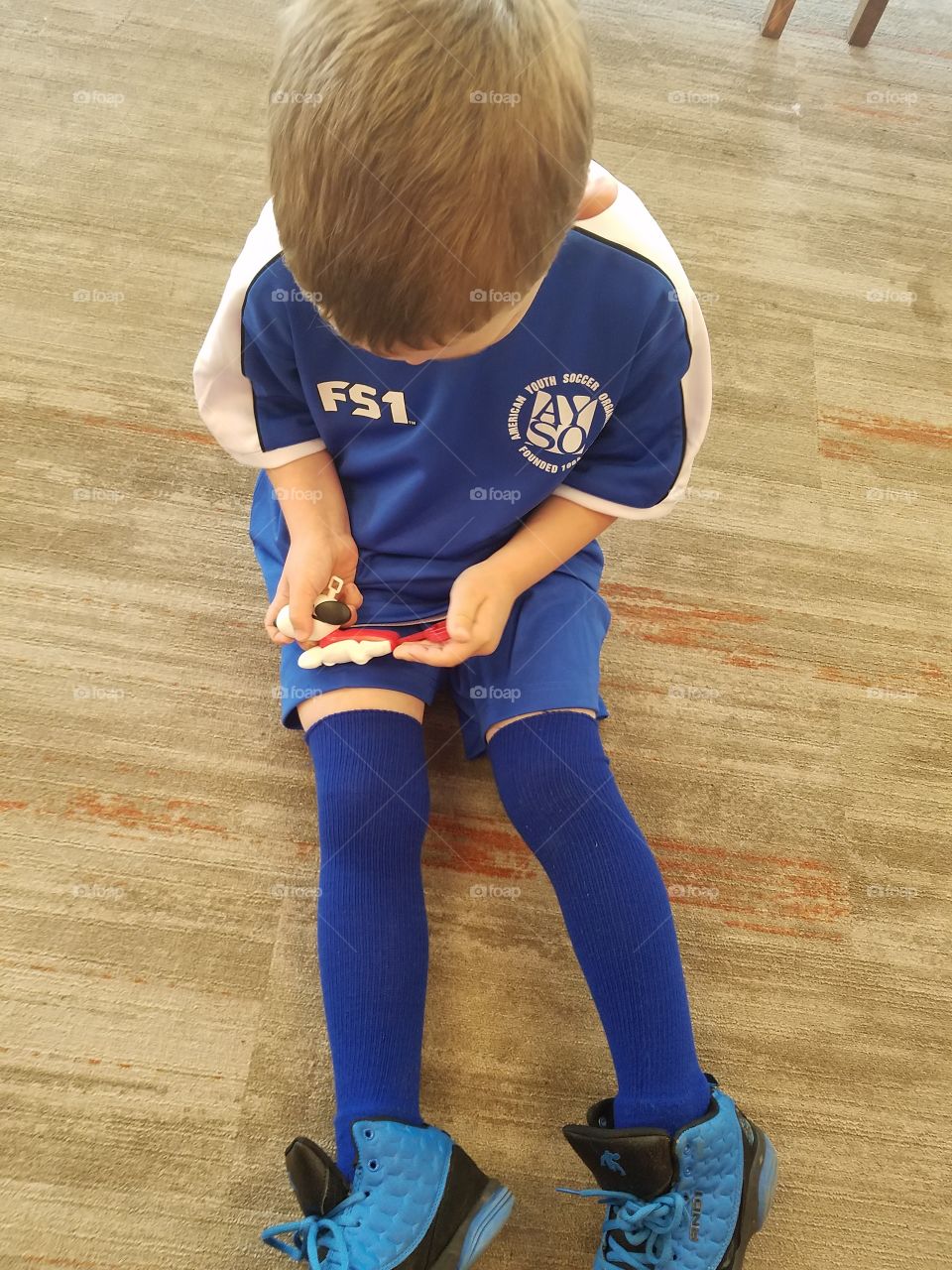 Blonde boy, in blue soccer uniform, sits on the floor and plays with snoopy toy.