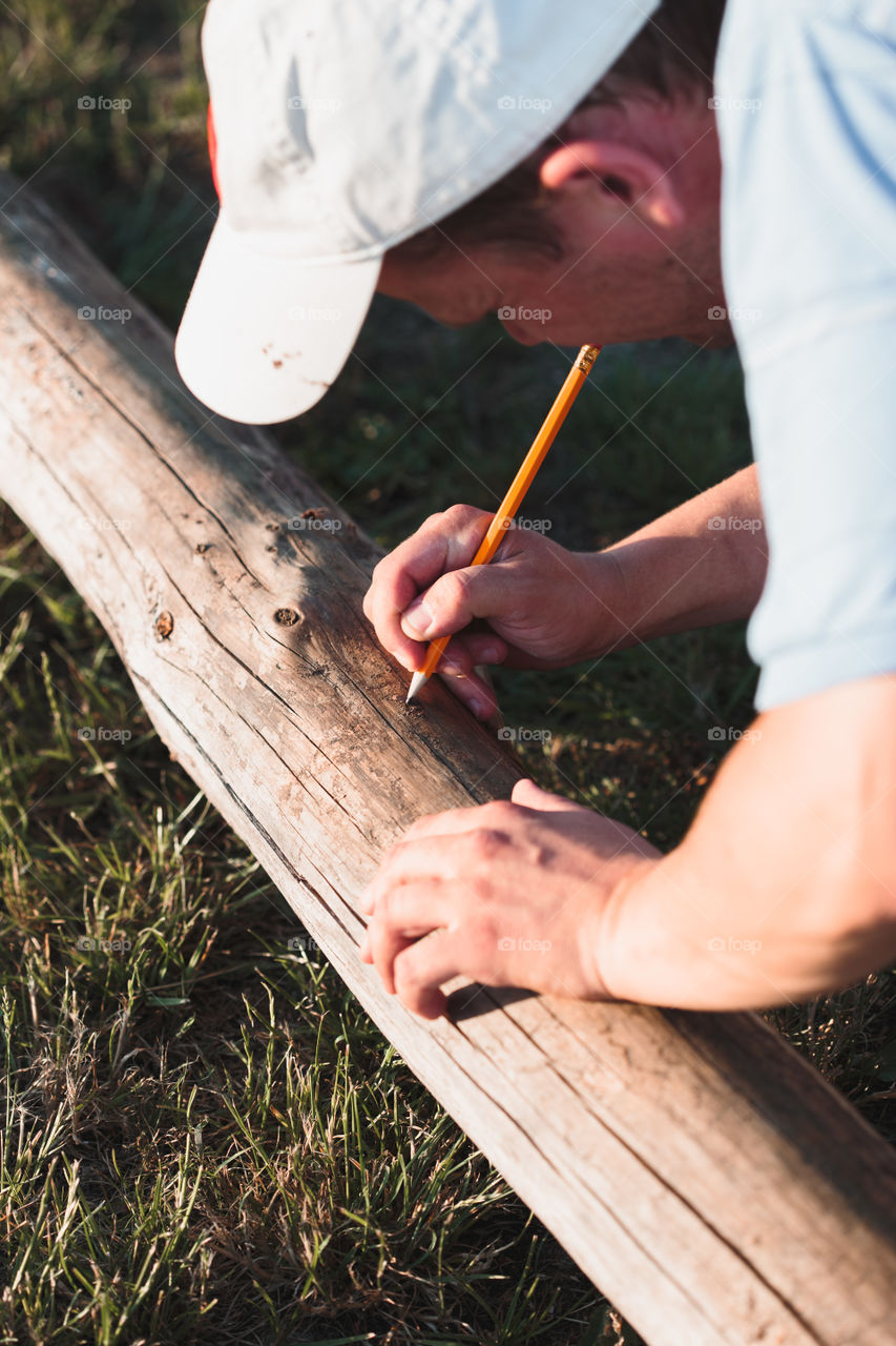 Man making mark by  using pencil after measuring of timber while working in garden