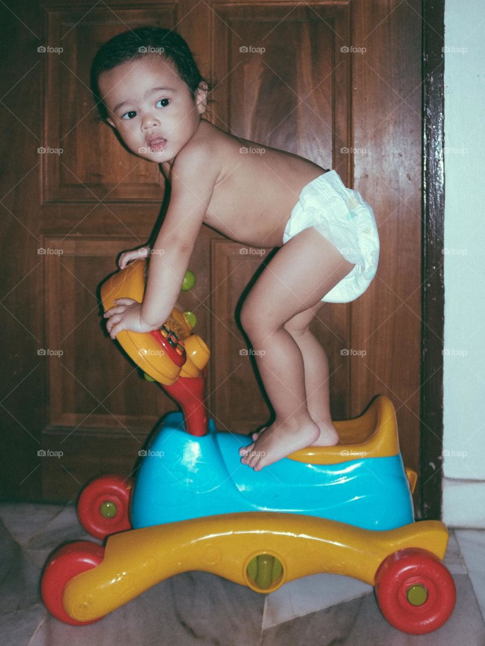 A polaroid style photo of a toddler standing on his musical bike