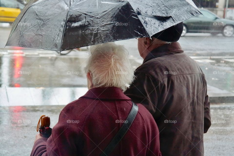 Elderly couple standing under umbrellas 