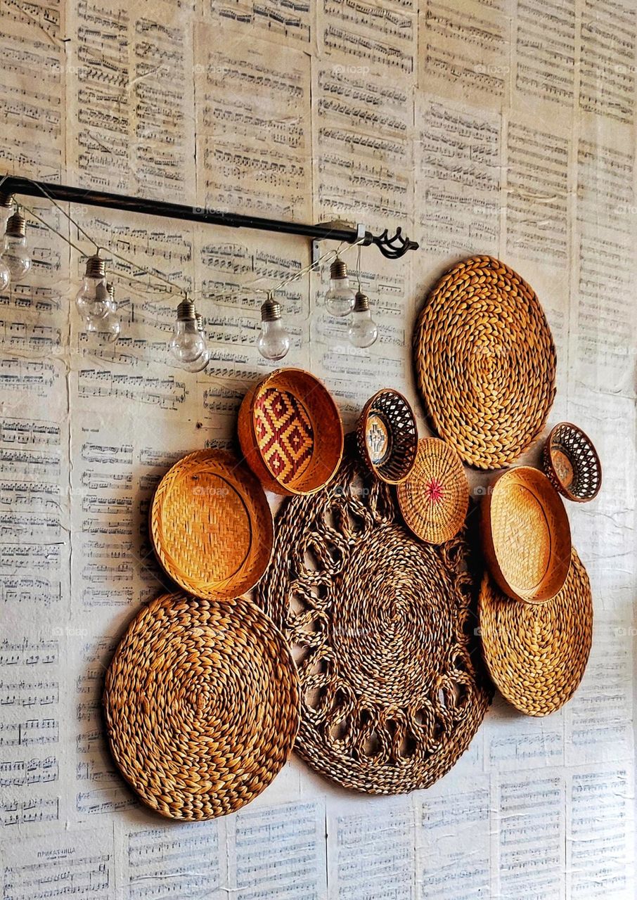 An amazing photograph of wall decoration consisting of circular knitted plates in different sizes, hanging light bulbs and wallpaper made of music notes sheets