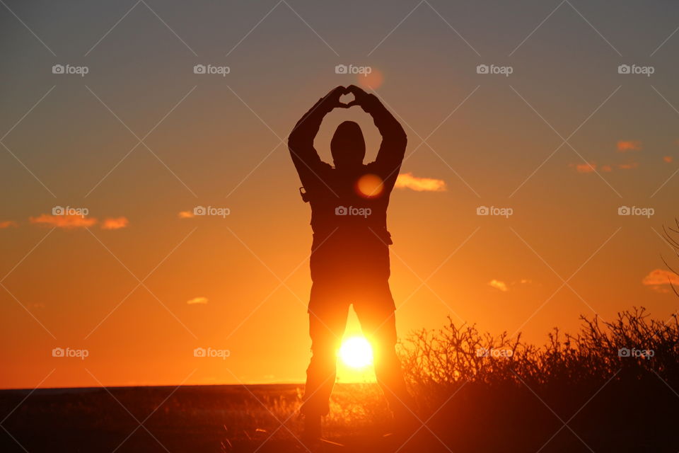 Man making heart shape with hands during sunset
